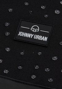 Fekete szövet táska vízcseppekkel, textúrált felülettel és egy téglalap alakú logóval, rajta fehér betűkkel a "JOHNNY URBAN" felirattal.