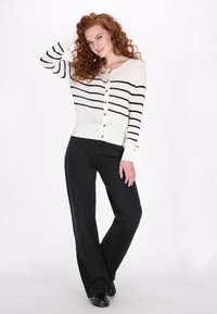 Witte gebreide cardigan met zwarte strepen, knoopsluiting aan de voorkant en geribde manchetten, gecombineerd met zwarte wijde broek en zwarte schoenen.