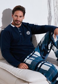 Navy-langärmliges Henley-Shirt mit Knopfleiste und Logo, kombiniert mit karierter Flanell-Pyjama-Hose in Blau, Weiß und Schwarz.