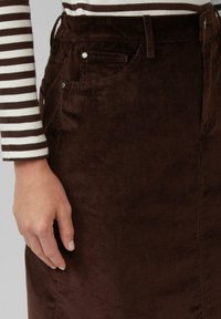 Bruine corduroy rok met verticale ribbels, zijzakken en metalen accenten. Gepaard met een gestreept lange mouwen top.