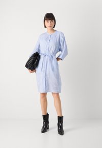 Svetlo modra lanena obleka z gumbom spredaj, 3/4 rokavi in zavezanim pasom. Združena z teksturirano črno usnjeno torbo in črnimi gležnjarji.