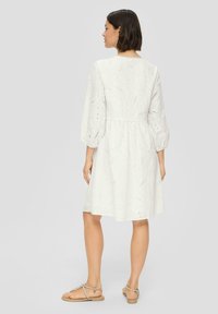 Robe en coton blanc avec des manches bouffantes, motif broderie anglaise, et une taille cintrée. Longueur genoux avec une coupe décontractée et une texture légère.