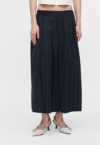 Femme portant un pantalon noir à jambes larges avec un petit motif à pois et des chaussures slingback blanches à talons bas avec boucles.