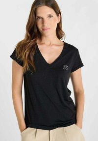 Zwart T-shirt met korte mouwen en V-hals, gemaakt van zachte stof, met een klein wit logo op de linkerborst. Simpel en casual ontwerp.