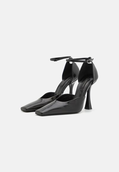 Sorte patentlæder højhælede sko med spids tå, ankelrem og en slank stiletto hæl. Glat tekstur med minimal detaljer.