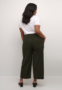 Pantalons larges verts avec une taille élastique, dotés de poches latérales. Associés à un simple t-shirt blanc et des sandales à talons carrés noires.