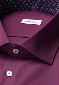 Camicia da uomo color prugna con colletto, bottoni bianchi e tessuto interno del colletto a motivo circolare rosso e bianco.
