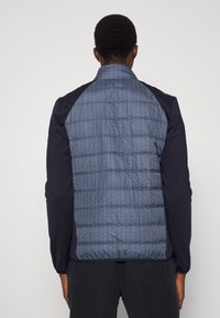 Padded jacket featuring a heathered blue back, dark blue sleeves, and a textured pattern. Designed for warmth with a cozy fit.
