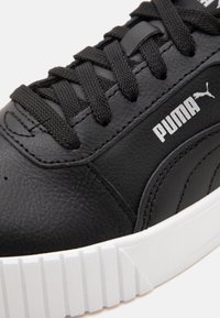 Zbliżenie na czarny sneaker Puma z teksturowaną skórą, czarnymi sznurowadłami, białym logo Puma i grubą białą żebrowaną gumową podeszwą.