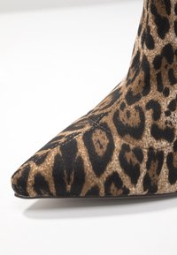 Botte à bout pointu en imprimé léopard avec une texture en tissu, présentant des nuances de brun et de noir. Silhouette élégante et finition lisse, sans matériel visible.