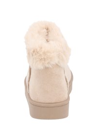 Beige faux mockasinstövlar med en fluffig, texturerad krage och en flat gummisula. Mjuk, plyschinredning för komfort.