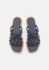 Marineblå flate sandaler med flere sammenvevde PVC-stropper, firkantet tådesign og beige gummisåle. Merkevaren sitt logo er preget på fotengen.