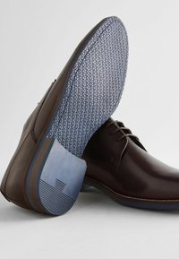 Braune Lederschuhe mit einem strukturierten blauen Fußbett, das ein hexagonales Muster aufweist, und einer strukturierten Gummisohle für besseren Halt.