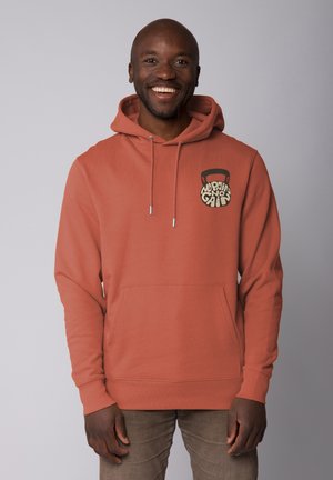 Hooded sweatshirt in clay orange fabric with a front pocket. Features a printed kettlebell logo in black and cream on the left chest.