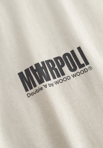 Μαύρο κείμενο «MAWRPOLI» με στυλιζαρισμένο γράμμα Α, ακολουθούμενο από «Double A by WOOD WOOD» τυπωμένο σε ανοιχτό μπεζ ύφασμα.