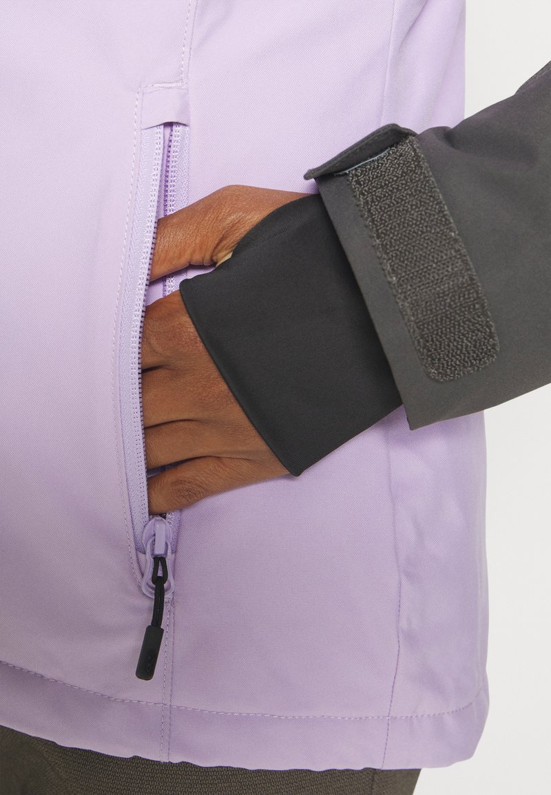 Helle lila Jacke mit einem seitlichen Reißverschluss und schwarzem Bund. Der Stoff wirkt glatt, mit matter Oberfläche und minimalen Nähdetails.