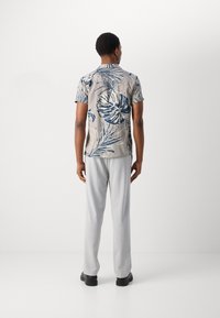 Cămașă cu mânecă scurtă, dintr-un material bej deschis, cu modele de frunze tropicale albastre, asociată cu pantaloni gri deschis și pantofi negri.