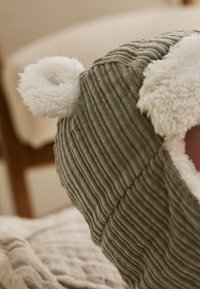 Zelená rebrovaná čiapka z mäkkého materiálu, s bielymi nadýchanými detailmi na vnútri uší na vrchu.