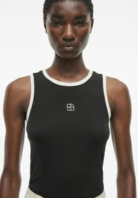 Zwarte mouwloze tanktop met een ronde halslijn, contrasterende witte afwerking en een klein wit logo op de borst. Gladde, passende stof.