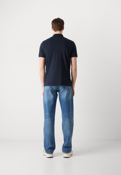 Polo shirt marine et jeans bleu clair, design ajusté, en coton, style décontracté, couture visible, porté avec des baskets beige.