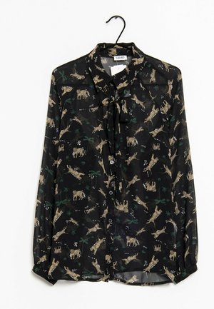 Blouse noire transparente à manches longues avec boutons sur le devant, col noué, et motif beige de tigre et feuilles vertes, suspendue sur un cintre noir.