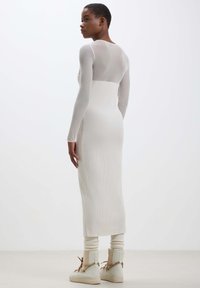 Abito a maniche lunghe in maglia a coste di colore beige chiaro con una silhouette aderente. Presenta una parte superiore semi-trasparente e una parte inferiore solida.