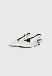 Białe, niskie buty na obcasie typu slingback z ostro zakończonym noskiem i złotymi klamrami, pokazane obok siebie na białym tle.
