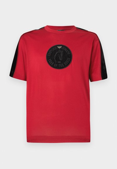 Rdeča bombažna majica s kratkimi rokavi, črnimi žametnimi poudarki in okroglim črnim okrasom z letnico "2026" ter silhueto konja.