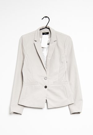 Light beige women's blazer with two buttons, notch lapels, and front pockets, hanging on a black hanger with visible brand tag and price tags.