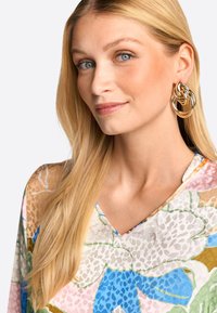 Feminine Bluse mit buntem Blumenmuster und V-Ausschnitt, aus leichtem Stoff gefertigt, in Pastelltönen von Rosa, Blau, Grün und braunen Akzenten.