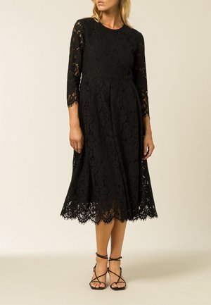 Robe en dentelle noire avec des manches longues, un corsage ajusté et une jupe midi évasée, avec un ourlet festonné et des détails de motif floral.