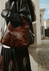 Torebka w leopardzi wzór wykonana z błyszczącego materiału imitującego skórę. Luźny kształt z wyciętym uchwytem, elementem jest mały zamek błyskawiczny.