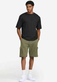Black cotton t-shirt paired with olive green cargo shorts featuring two side pockets. Worn with white sneakers and crew-length socks.