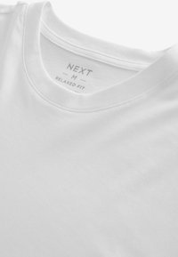Tricou din bumbac alb, croi lejer, guler rotund, cu margini cusute. Eticheta spune "NEXT M RELAXED FIT" cu un font gri subtil.