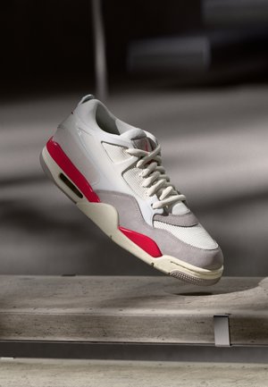 Sapatilha cinza-claro e branca com detalhes em rosa e malha texturizada. Apresenta um design aerodinâmico e sola de borracha com amortecimento de ar.