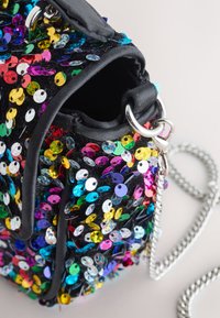 Juoda audinio rankinė su juodais blizgučiais, puošta įvairaus dydžio spalvotais blizgučiais, su sidabrine grandinėlės rankena ir minkšta, apvalia forma.