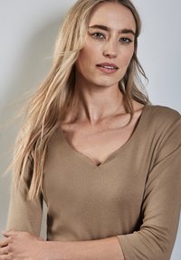 Maglietta marrone a maniche lunghe con un design a scollo a V profondo, texture morbida, forma aderente e maniche leggermente svasate. Minimalista, di colore solido senza motivi.