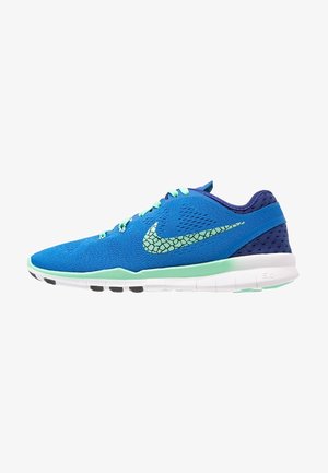 Chaussure de sport bleue avec lacets vert clair, virgule Nike vert clair à motifs, talon violet et semelle blanche avec détails noirs sur la semelle.