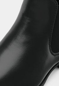 Botine Chelsea din piele neagră netedă, cu panou elastic pe lateral și vârf rotund, prezentate în prim-plan pe un fundal alb.