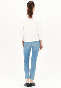 Witte langemouwen top, denim jeans in lichtblauw, aansluitend ontwerp, achterkant zicht, eenvoudige halslijn, subtiele stiksels, gedragen met zwarte platte schoenen.