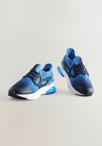 Baskets de sport bleues avec un mélange de textures mates et brillantes, matériaux en mesh et synthétiques, amortissement de semelle proéminent et designs en couches.