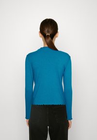 Ribbad långärmad topp i livfull blå färg, med en vågig nederkant och rund halsringning. Tyget är slätt med en lätt stretch.