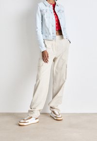 Light blue denim jacket over a red cropped top with white polka dots, paired with beige cargo pants and white sneakers with brown accents.