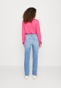 Blusa rosa de manga larga con yugo trasero, combinada con jeans rectos de pierna clara con bolsillos traseros y un lavado desgastado.