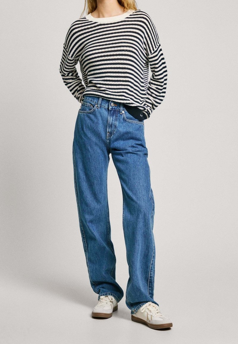 Randig stickad tröja i svart och vitt, matchad med lös passform i blå jeans. Sneakers i vitt med ljusbruna sulor. Enkel, avslappnad outfit.