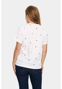 T-shirt en coton blanc à manches courtes, avec un motif de cœurs dispersés en bleu marine au dos. Coupe simple et décontractée.