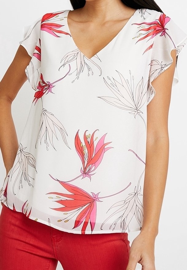 Blusa bianca con scollatura a V, maniche a farfalla corte e motivo floreale rosa su un tessuto leggero. Abbinata a pantaloni rossi uniti.