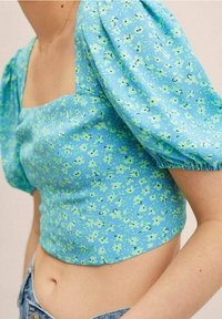 Hellblauer, floral gemusterter Crop-Top mit kurzen Puffärmeln, ausgestattet mit einem quadratischen Ausschnitt, aus strukturiertem Stoff mit grünen Blumenmustern.