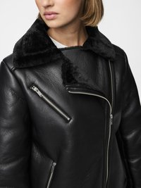 Black leather jacket featuring a fur-lined collar, silver zippers, and a textured finish. Close-up view highlights the design details.