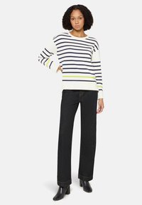 Sweter w granatowo-białe paski z zielonym akcentem, zestawiony z czarnymi wysokim stanem jeansami i czarnymi botkami na obcasie.